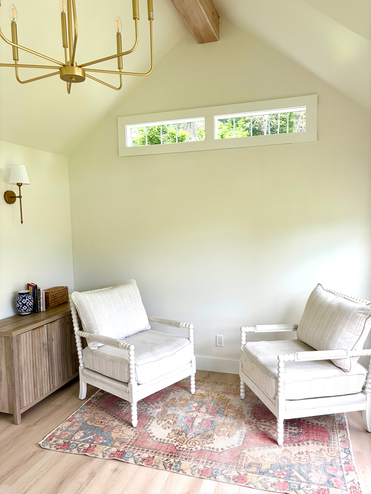 Studio sitting area — two white chairs on a vintage rug under a brass chandelier