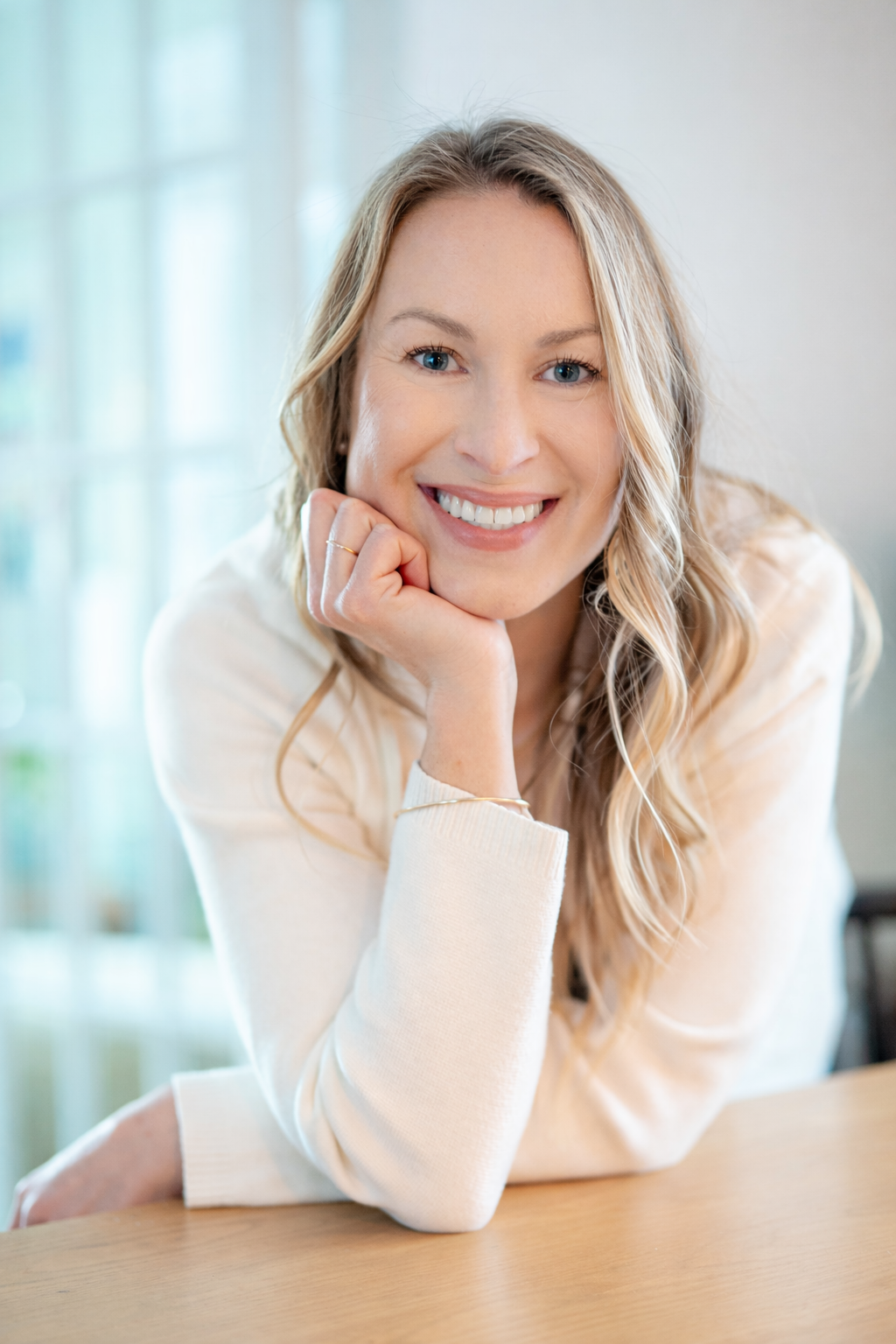 Maura Reminga portrait — smiling, resting her chin on her hand in a light-filled room